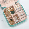 A pink leather jewelry travel organizer box filled with various gold and silver rings, earrings, and necklaces.