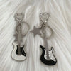 Guitare argentée et clés en forme de cœur suspendues à un charm étoile sur fond blanc moelleux