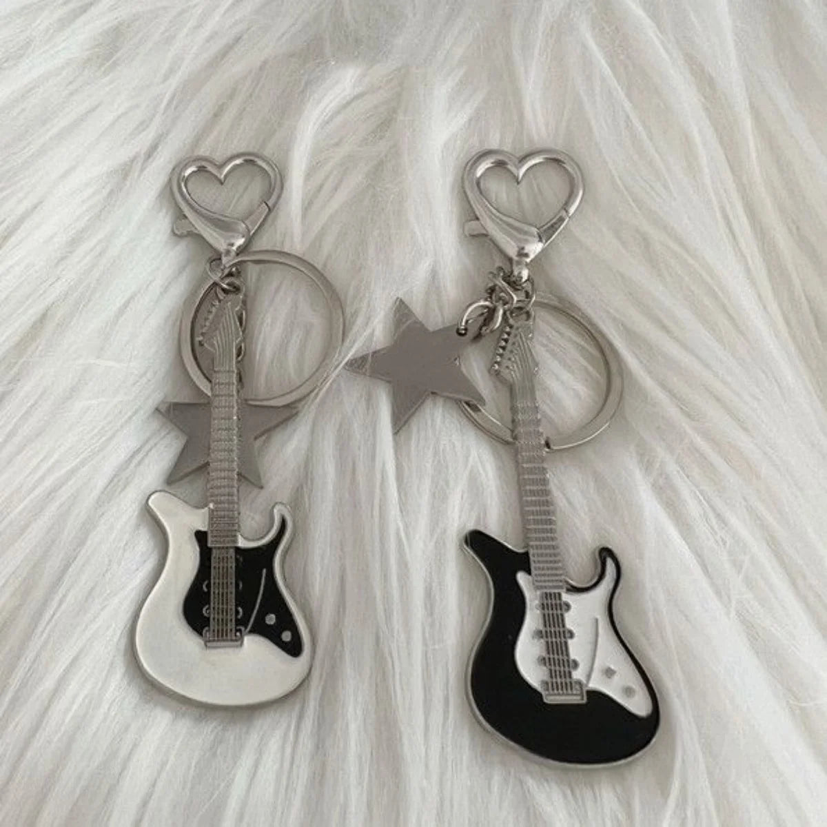 Guitare argentée et clés en forme de cœur suspendues à un charm étoile sur fond blanc moelleux