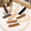 A set of rubber braided ponytail holders and scrunchies in various shades of brown, beige, and white displayed on a white pla