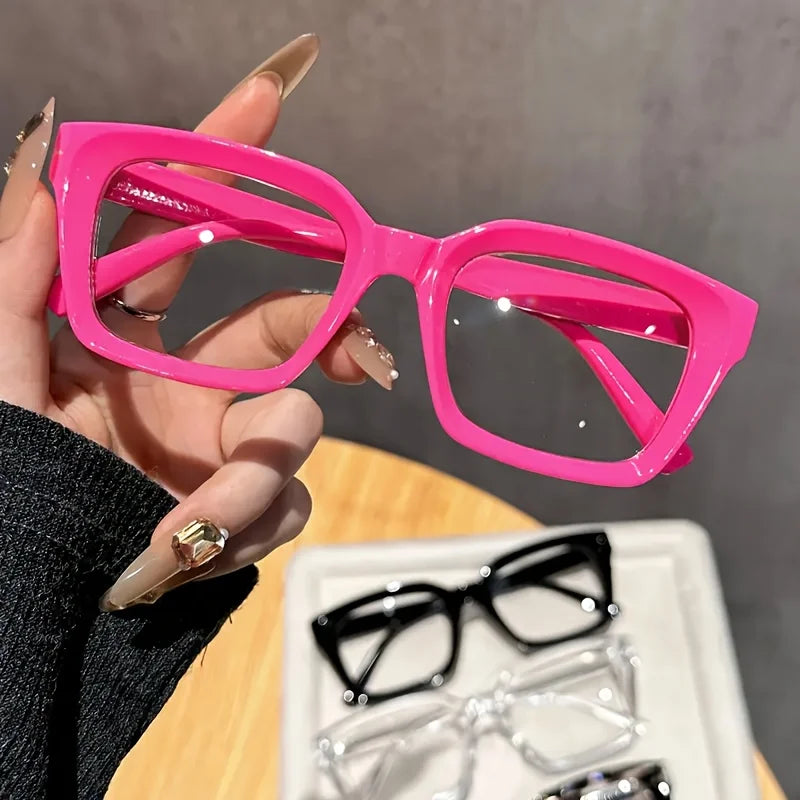 A hand holds a pair of bright pink, thick-framed square reading glasses against a neutral background.