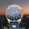 A close-up of a men's luxury quartz sport watch with a blue dial and gold accents, set against a cityscape background.
