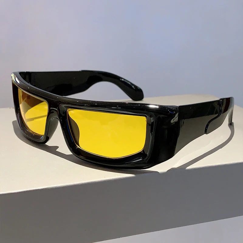 Un par de gafas de sol negras con montura metálica y lentes amarillo brillante sobre una superficie blanca.