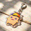 A clear acrylic keychain featuring a stylized, smiling face wearing an orange and yellow hat.
