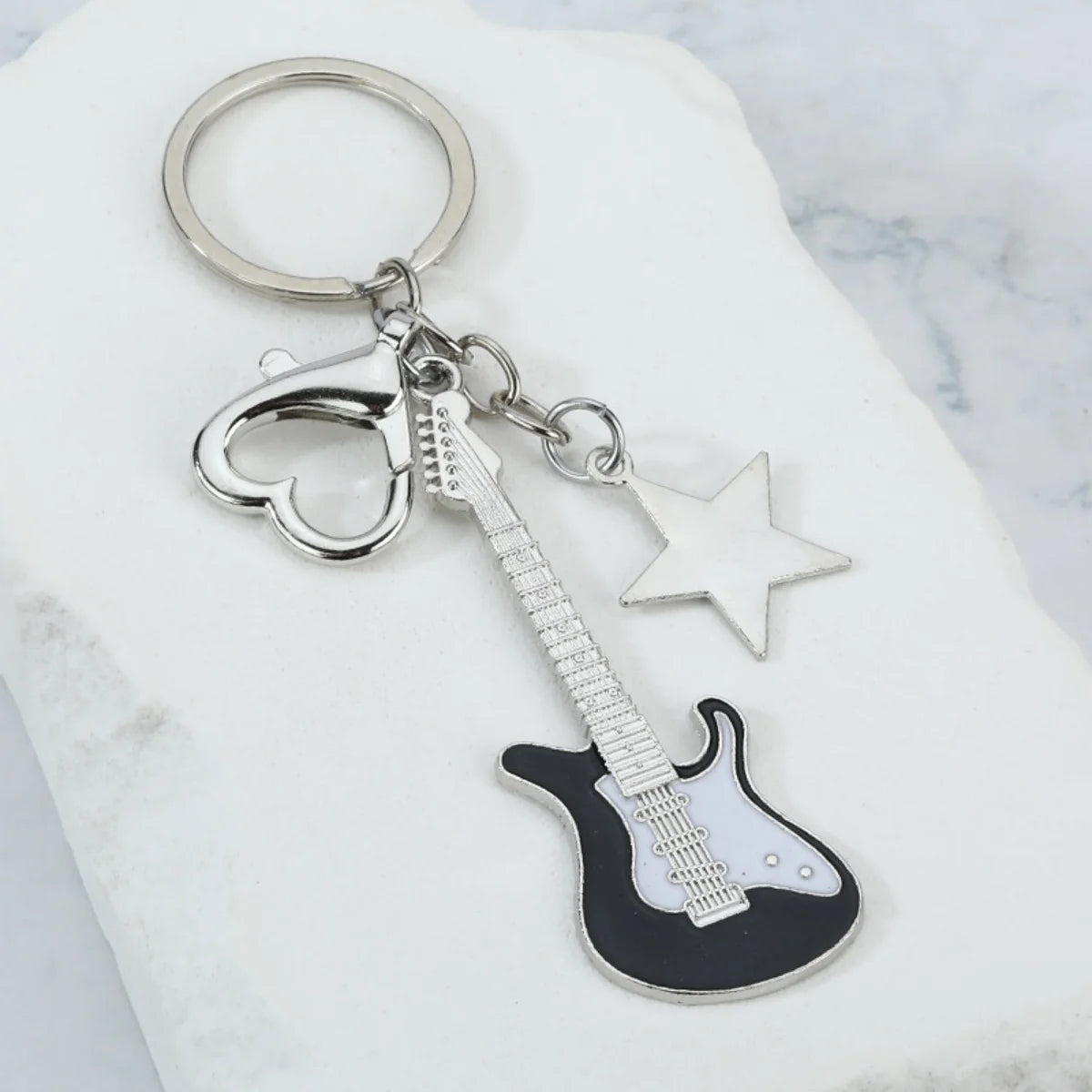 Clé-pendant de guitare argentée avec cœur et étoile sur fond de marbre blanc
