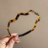 Una mano sostiene unos aros de pelo retro de acetato ondulado color tortuga contra un fondo neutro.