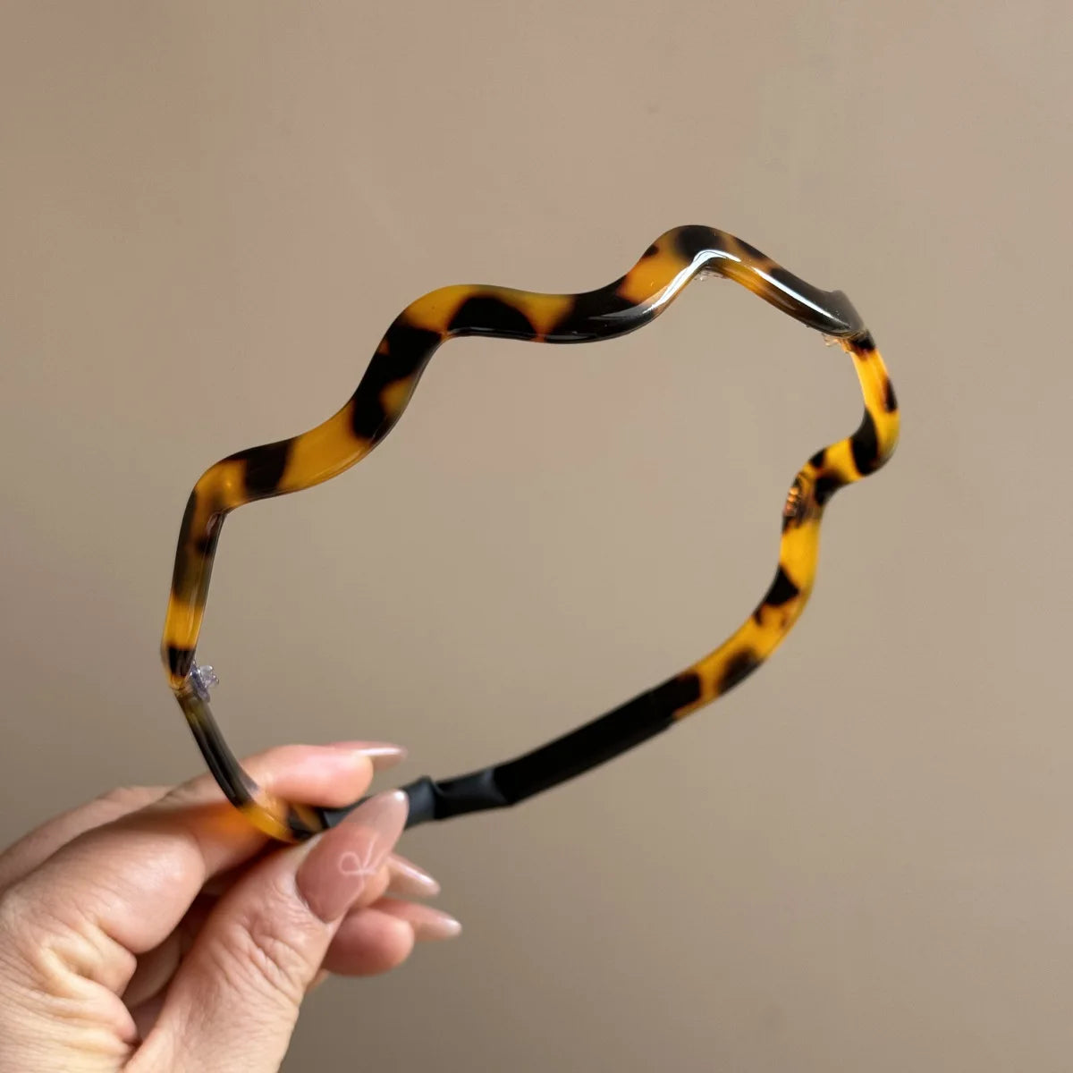Una mano sostiene unos aros de pelo retro de acetato ondulado color tortuga contra un fondo neutro.