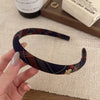 A hand holds a dark blue and maroon plaid fabric headband with a gold accent on a light surface.