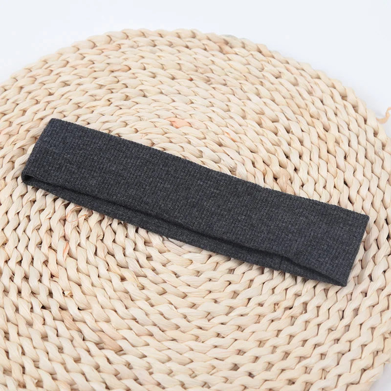 A dark gray knitted elastic headband lying on a natural woven mat.