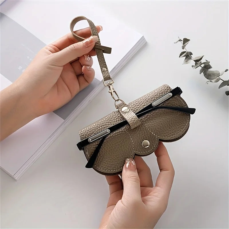 A hand holds a brown PU leather eyewear pouch and glasses case with a leather strap.