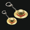 A pair of anime style straw hat metal keychains with gold and red accents.