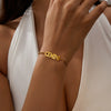 A close-up of a hand wearing a gold stainless steel Zodiac constellation charm bracelet on a white dress.