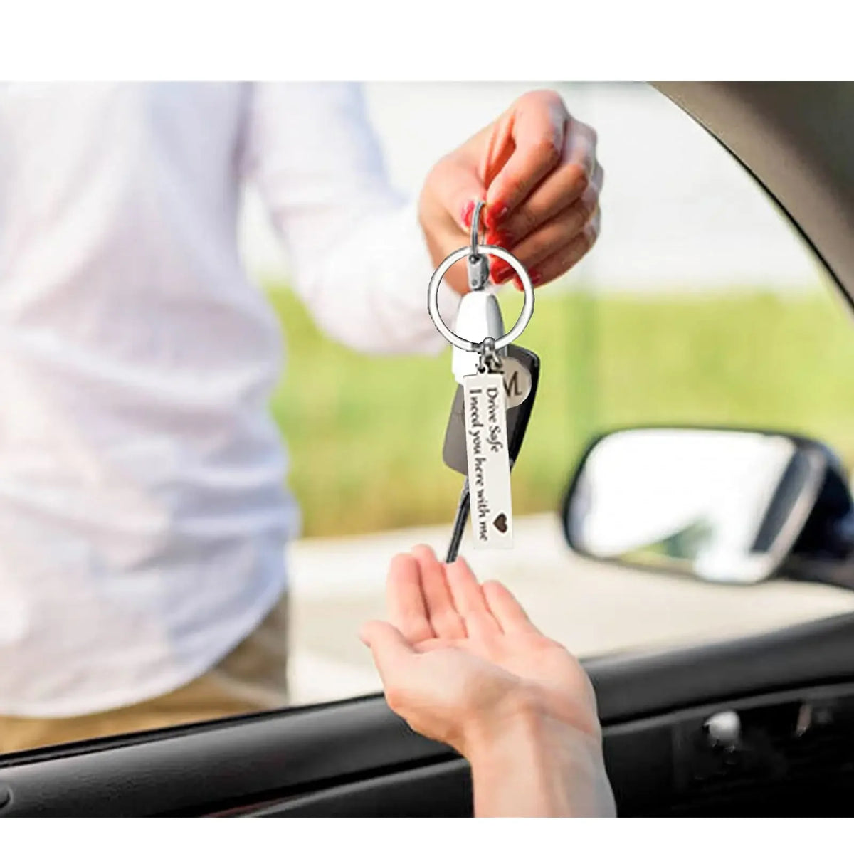 A hand is holding a personalized initial drive safe keychain, showing the key and tag against a car window.