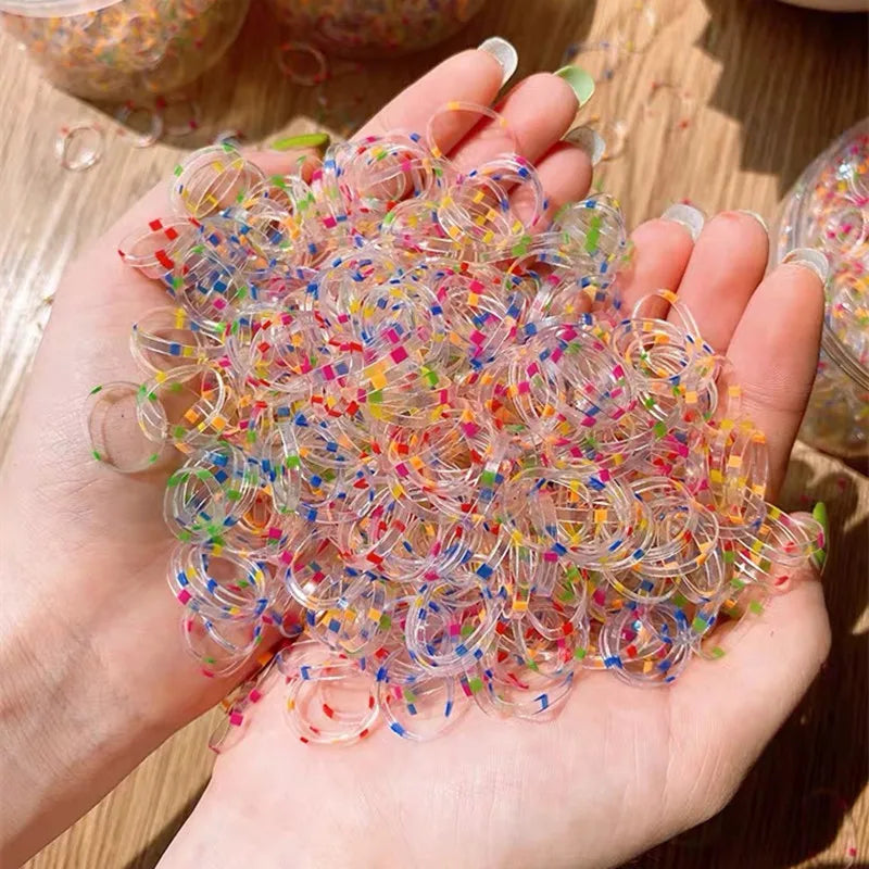 A hand holds a large pile of colorful disposable hair scrunchies for ponytail holders.
