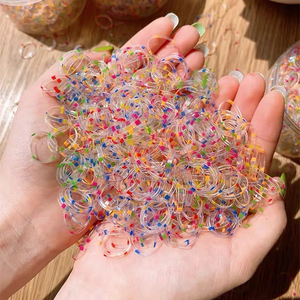 A hand holds a large pile of colorful disposable hair scrunchies for ponytail holders.