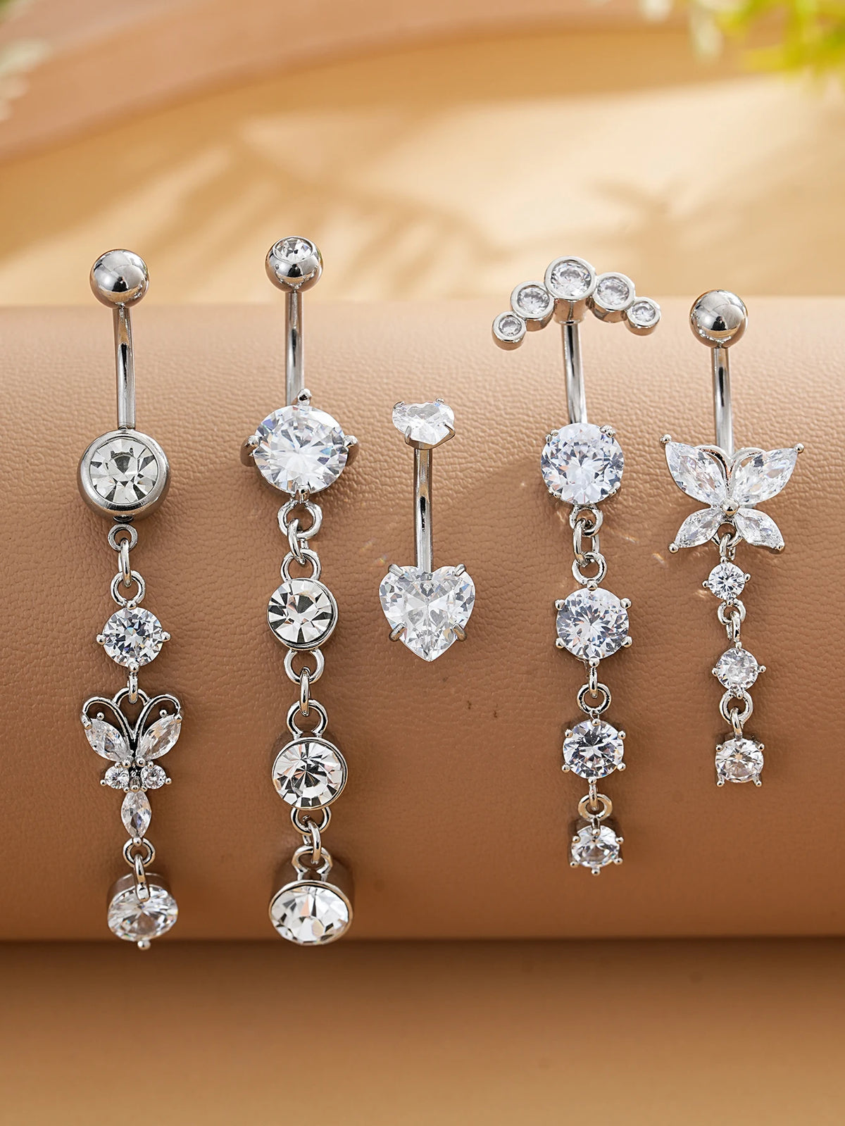 A set of five gold stainless steel dangled belly button rings featuring various diamond and floral designs.