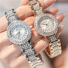 A hand holds a sparkling gold-toned watch with a clear face and rhinestone accents.