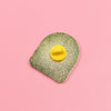 A close-up of a gold glitter enamel brooch pin with a yellow enamel center on a pink background.