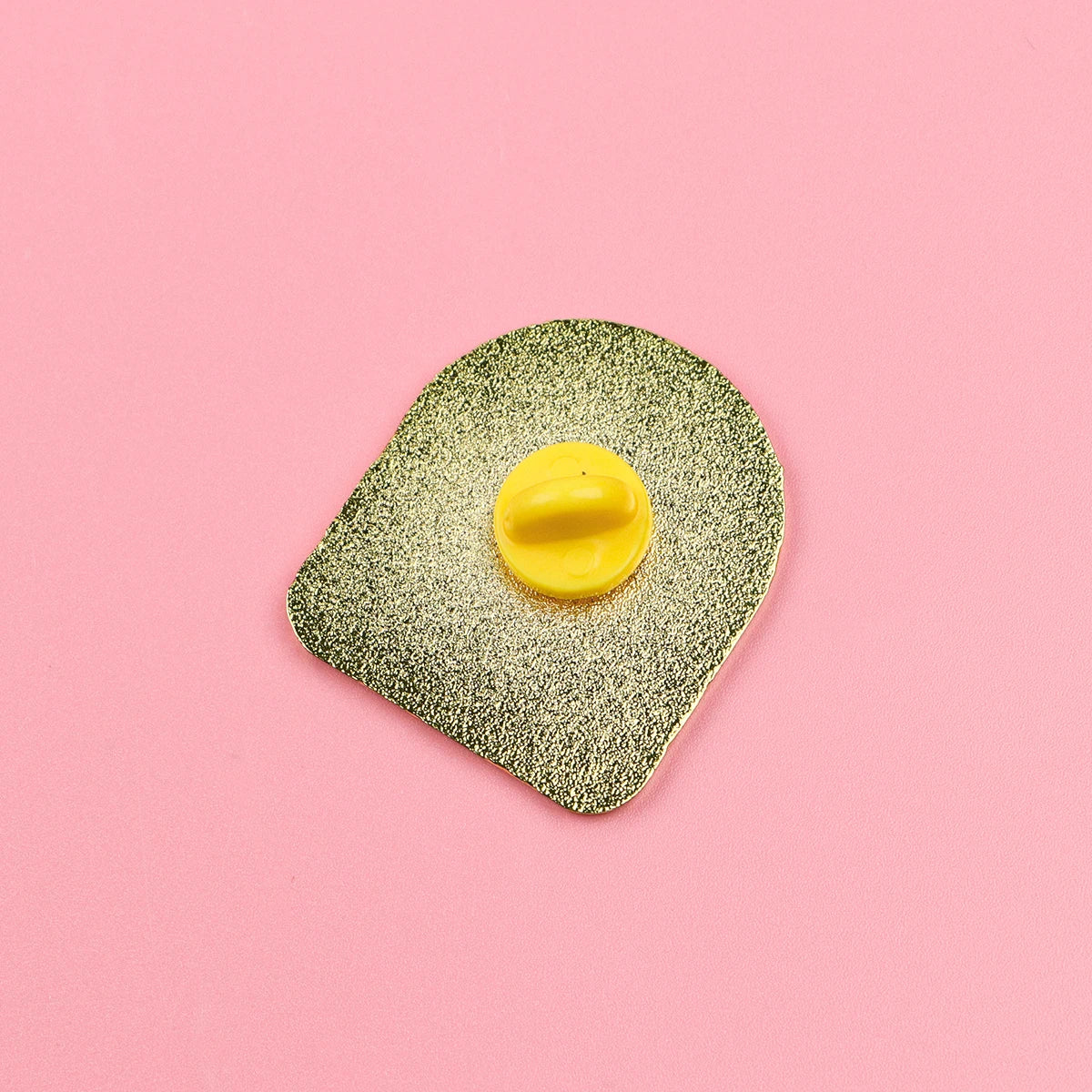 A close-up of a gold glitter enamel brooch pin with a yellow enamel center on a pink background.