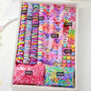 A box of colorful decorative hair accessories, including various colored elastic bands and charms, packaged with quantity lab