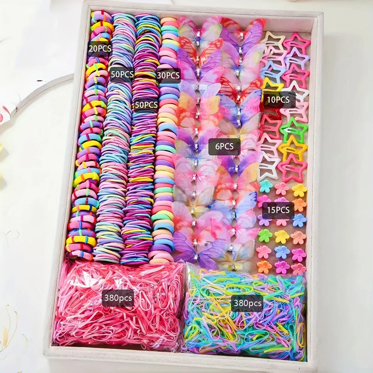A box of colorful decorative hair accessories, including various colored elastic bands and charms, packaged with quantity lab