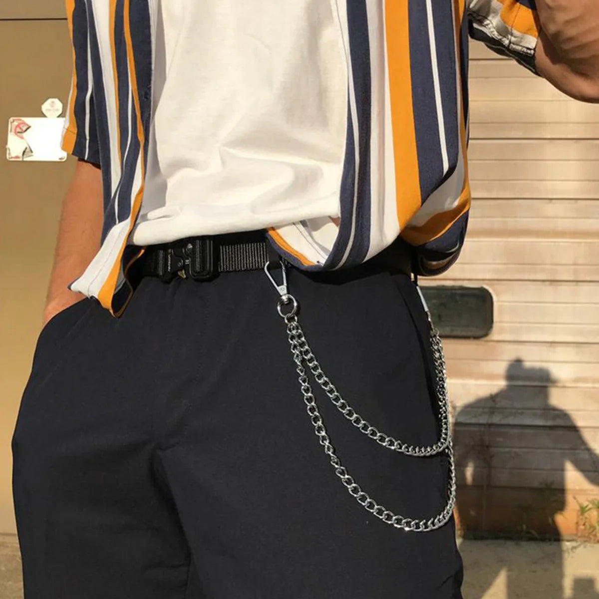 A person wearing dark blue jeans and a white shirt with striped sleeves, accessorized with a metal waist chain.