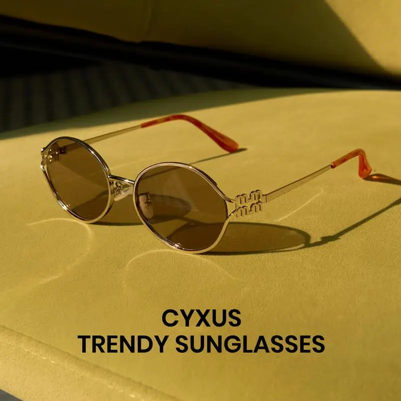 Ein Paar retro ovale Sonnenbrille mit goldenem Rahmen und getönten Linsen auf einer hellgelben Oberfläche.