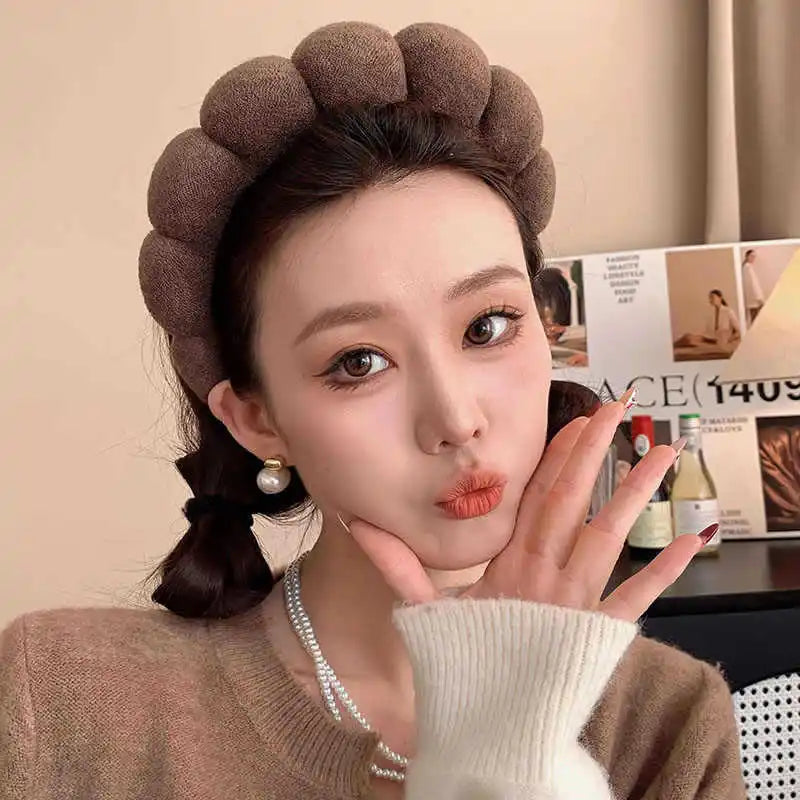 A woman models a brown cloud sponge hair accessory headband with a white sweater and pearl necklace.