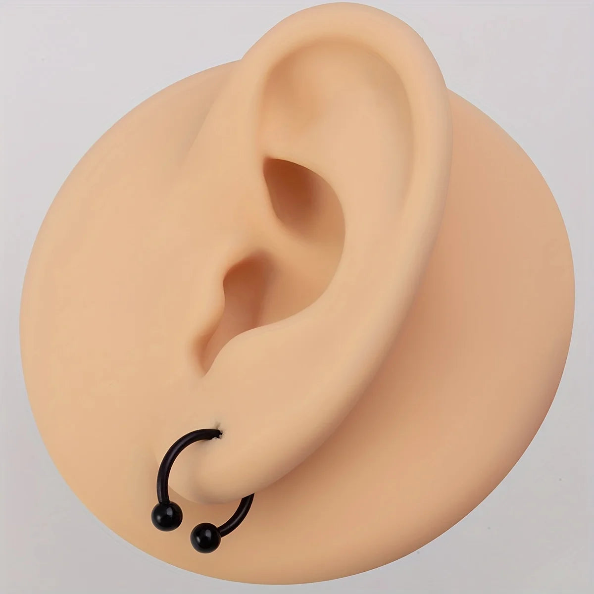 A light peach colored human ear model with a black hoop and bead piercing jewelry set.