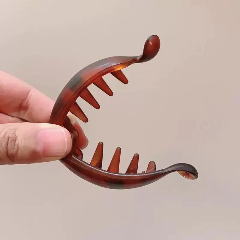 Una mano sostiene un clip de plátano marrón con varios dientes afilados, mostrando el producto para el cabello.