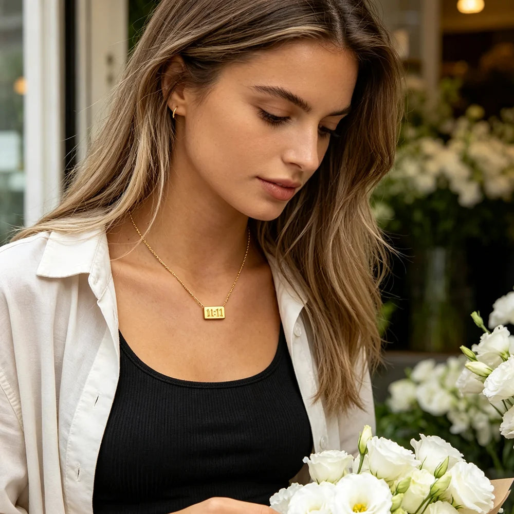 A woman wearing a white shirt and black top models an 18K gold plated rectangle pendant necklace.