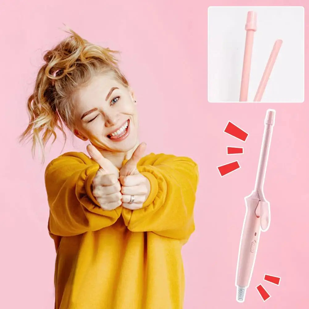 A woman with curly hair is smiling and making a peace sign while holding a pink ceramic curling iron and its interchangeable 