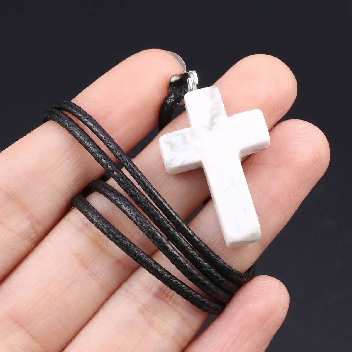Eine Hand hält eine schwarze Schnur mit einem Kreuz-Anhänger aus Tigerauge-Agat.