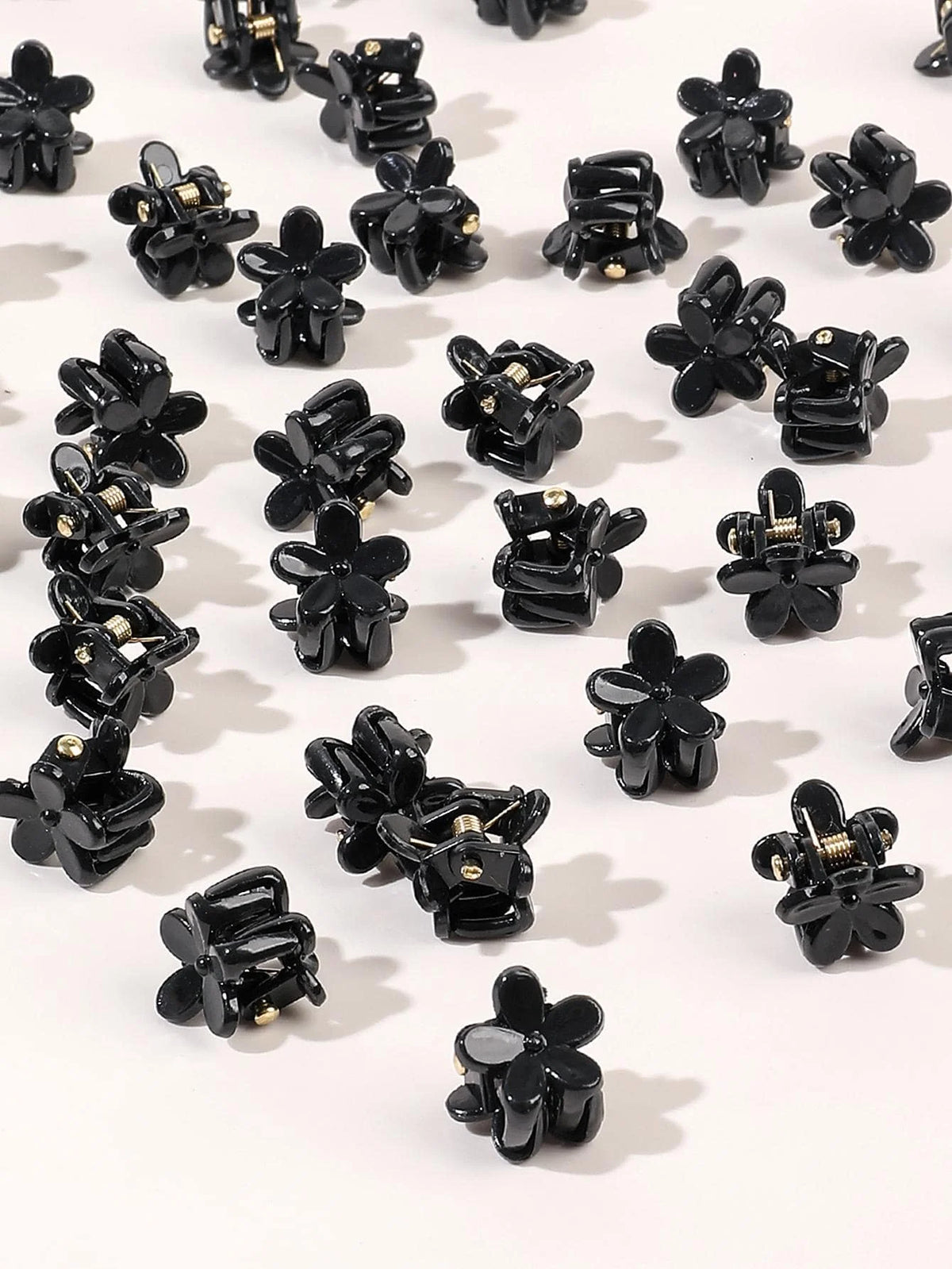 A set of black mini flower hair clips scattered on a white background.