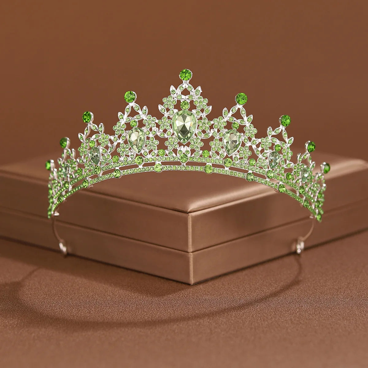 A sparkling crystal baroque bridal tiara with green stones and a central diamond set on a brown box.