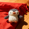 Peluche de pingüino gris y blanco esponjoso dentro de un estuche protector de tela roja.