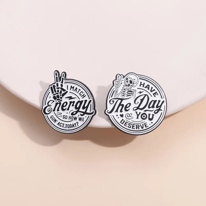 Two circular enamel lapel brooches featuring text related to matching energy and deserving the day