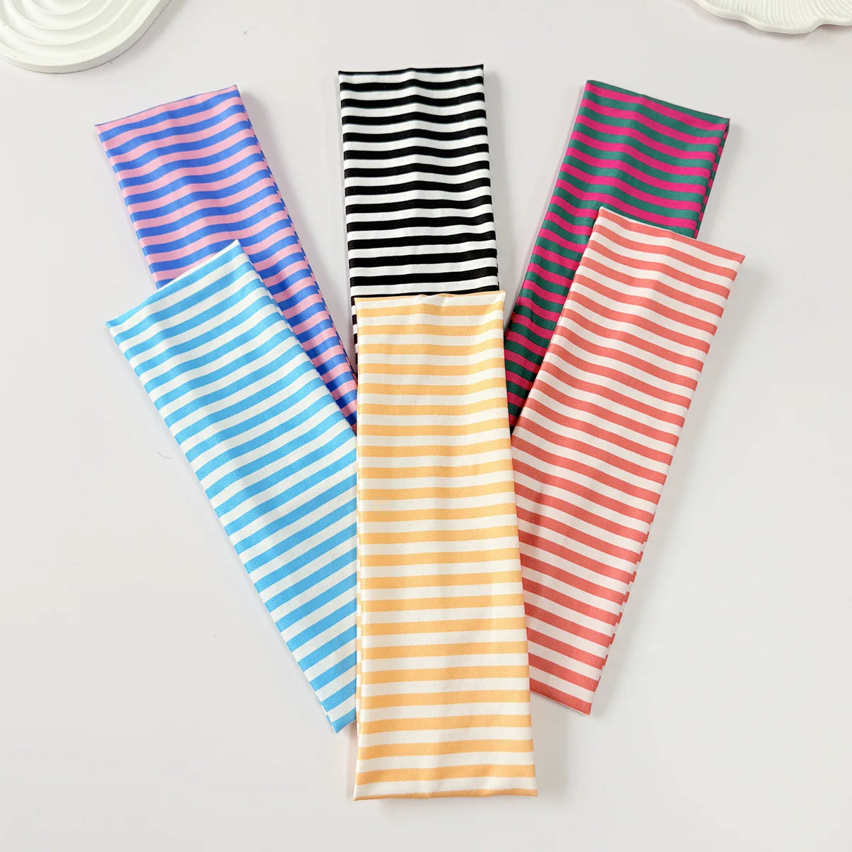 Une collection de bandeaux pour cheveux colorés à rayures, disposés sur une surface blanche.