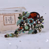 Broche florale en cristal élégante avec diverses pierres colorées et feuillage vert.