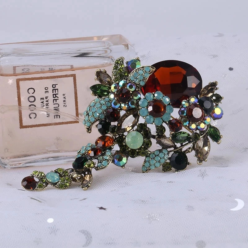 Broche florale en cristal élégante avec diverses pierres colorées et feuillage vert.