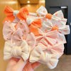 A hand holds a cluster of pink, white, and orange fabric flower bow hair ties for girls.