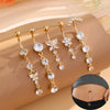 A set of five gold stainless steel dangled belly button rings with floral and crystal accents displayed on a beige fabric.