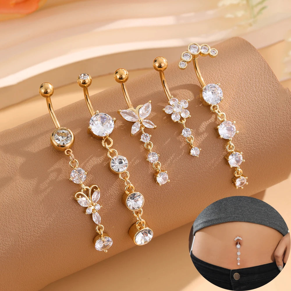 A set of five gold stainless steel dangled belly button rings with floral and crystal accents displayed on a beige fabric.