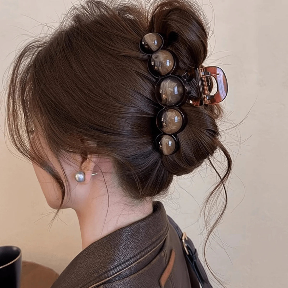 A close-up of a woman's dark brown hair styled in an elegant updo with acrylic pearl hair claw clips.