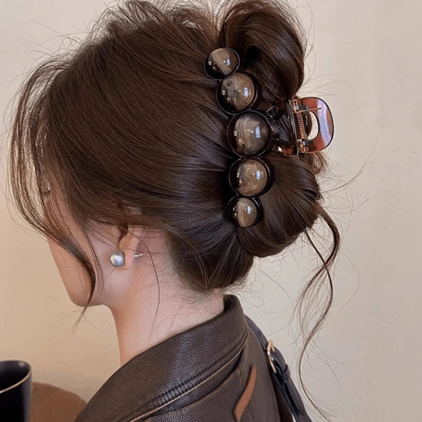 A close-up of a woman's dark brown hair styled in an elegant updo with acrylic pearl hair claw clips.