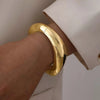 A close-up of a hand wearing a thick, gold cuff bangle bracelet on the wrist.