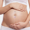 A woman's pregnant belly shows a delicate silver belly button ring with a pink gemstone.