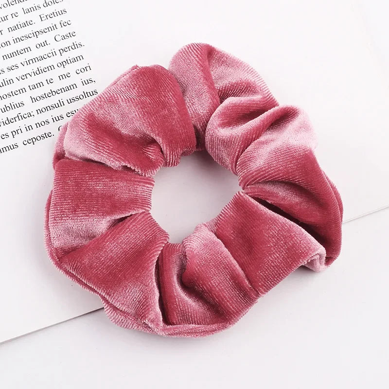 A close-up of a set of six dusty rose velvet scrunchies with gathered fabric texture on a white background.
