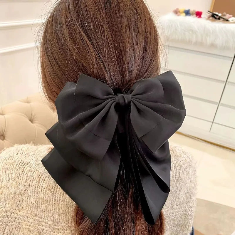 A black satin bow hair clip is tied into a large bow at the back of dark brown hair.