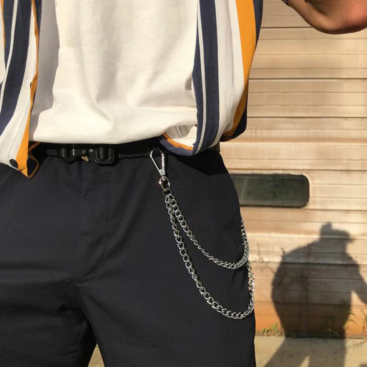 A person wearing black pants with a silver metal waist chain accessory.